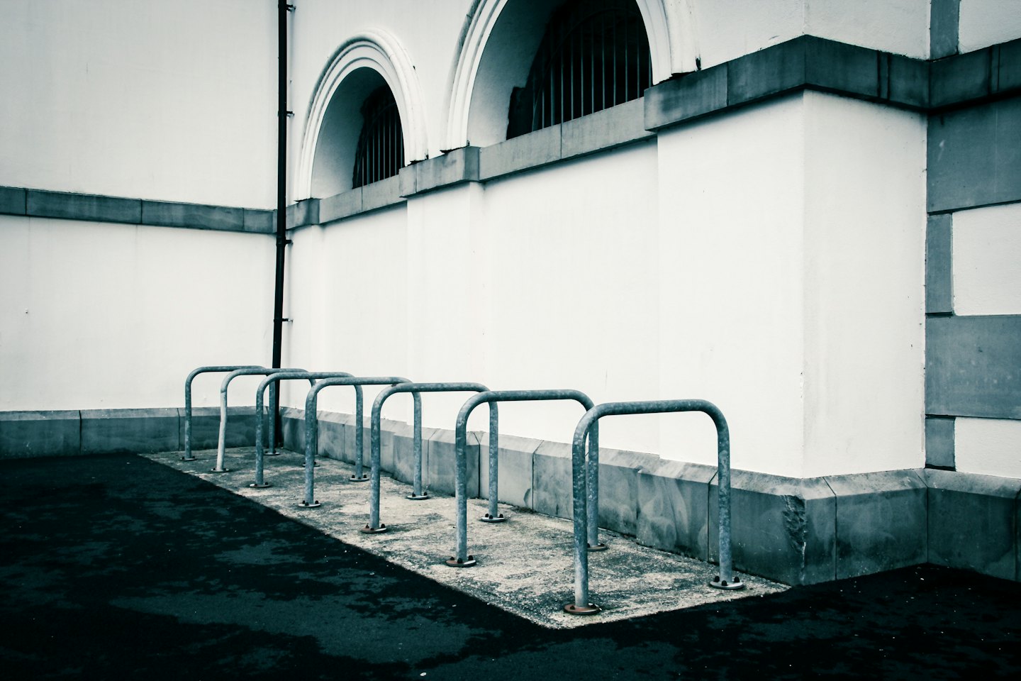 Empty metal bicycle racks stand against a white building wall.