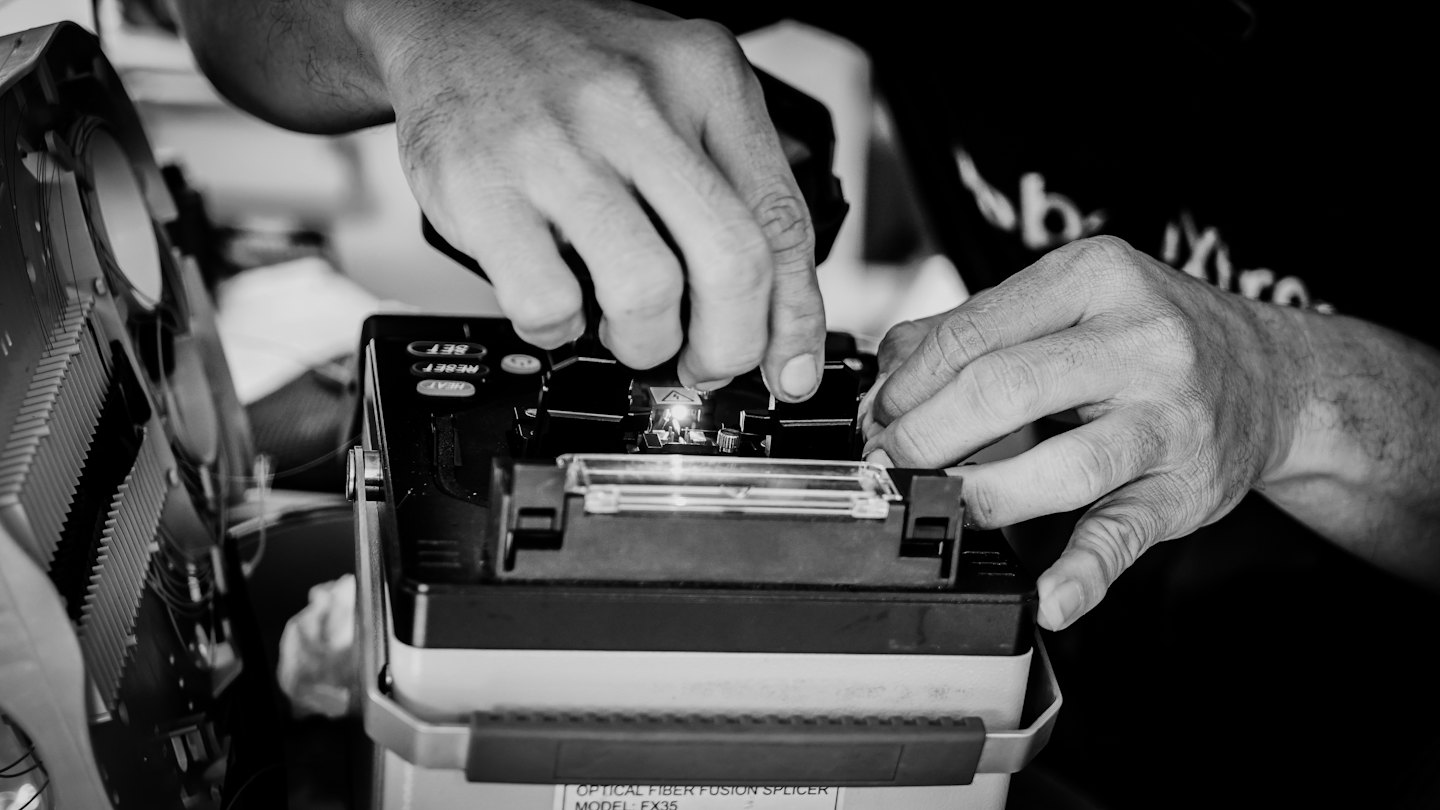 Technician hands using an optical fiber fusion splicer.