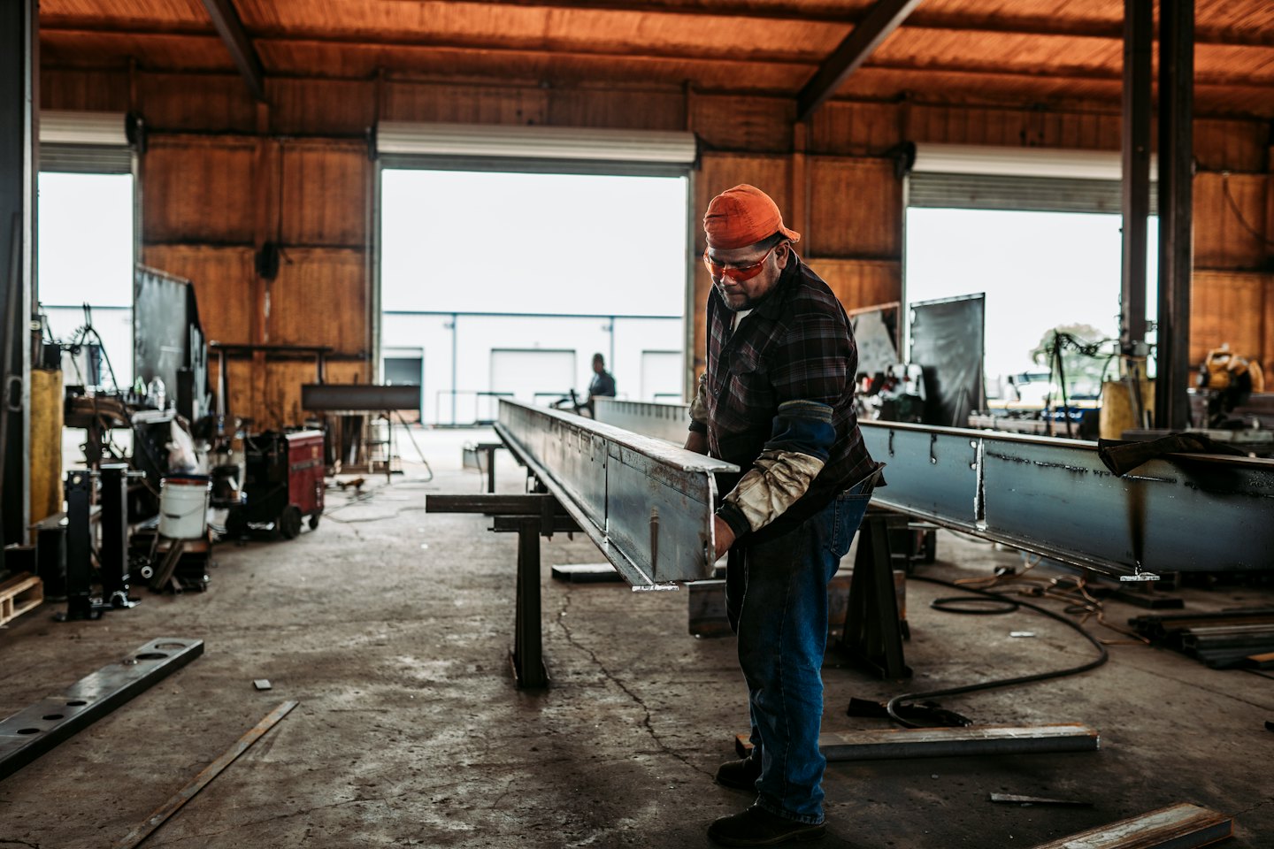 Man inspects a large steel I-beam in a workshop.