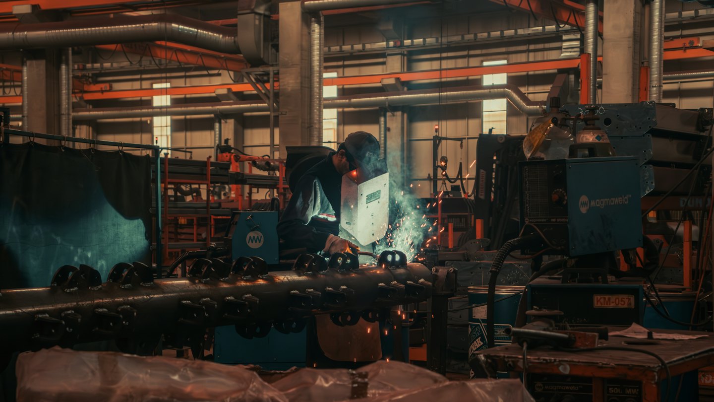 Welder in helmet creating sparks on metal in factory.